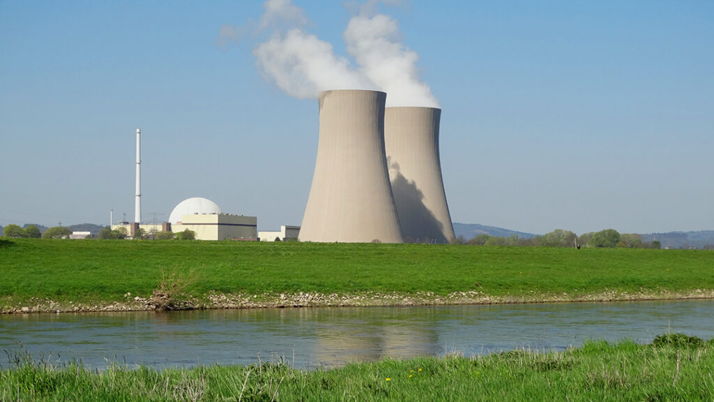 Ein Kernkraftwerk mit zwei markanten Schornsteinen vor einem strahlend blauen Himmel.