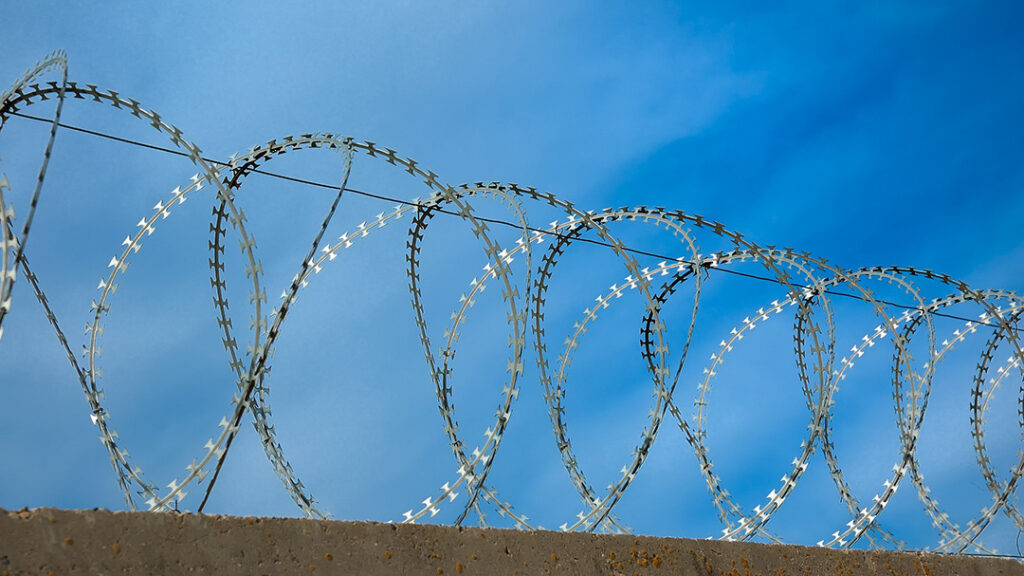 Stacheldrahtzaun unter einem blauen Himmel, der die Themen Sicherheit und Abgrenzung visuell vermittelt.